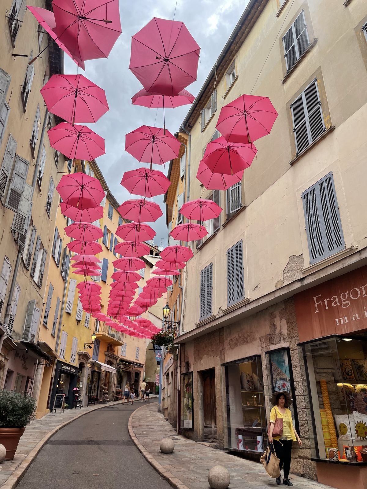Sucheta walking the Grasse perfume street under pink umbrellas, Fragonard shop in background